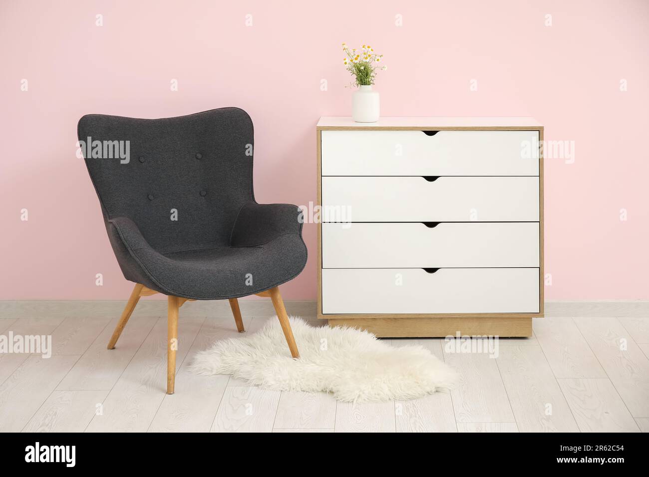 Dark grey armchair with dresser, fluffy rug and daisy near pink wall Stock  Photo - Alamy