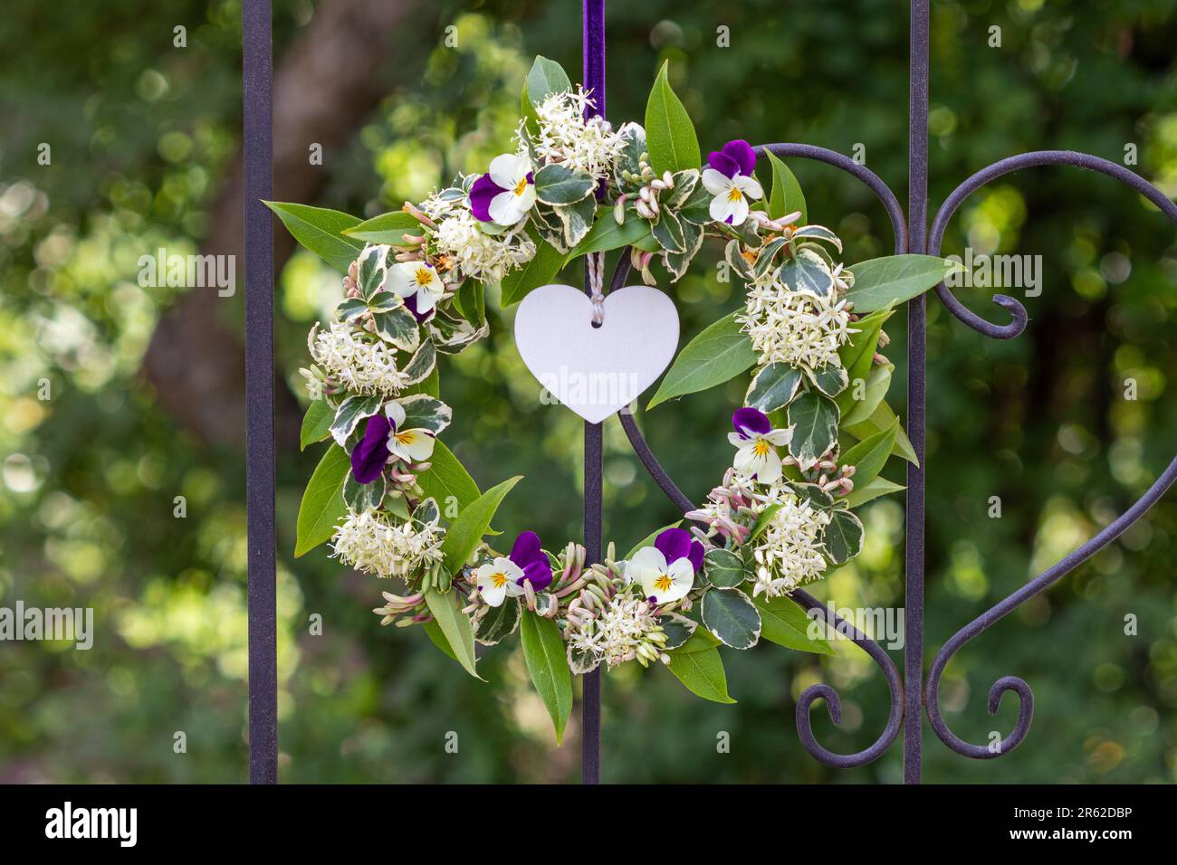 wreath of viola flowers, flowers of Siberian dogwood and honeysuckle hanging in garden Stock Photo