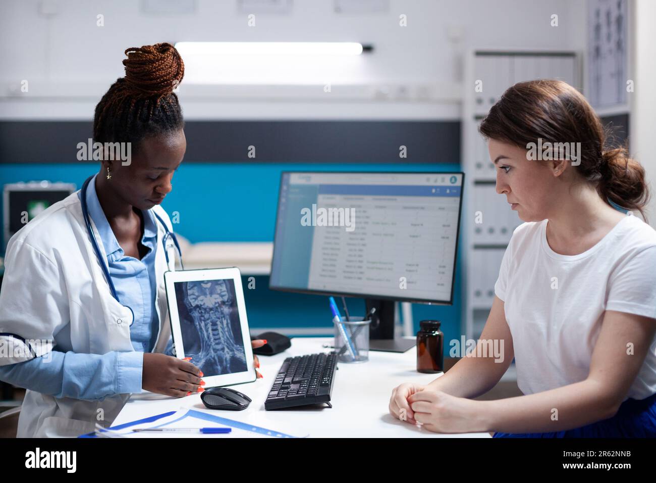 Doctor showing cervical vertebrae injury neck pain x-ray ct scan results on tablet to patient during medical appointment. Healthcare specialist diagnosing woman after symptoms checkup Stock Photo