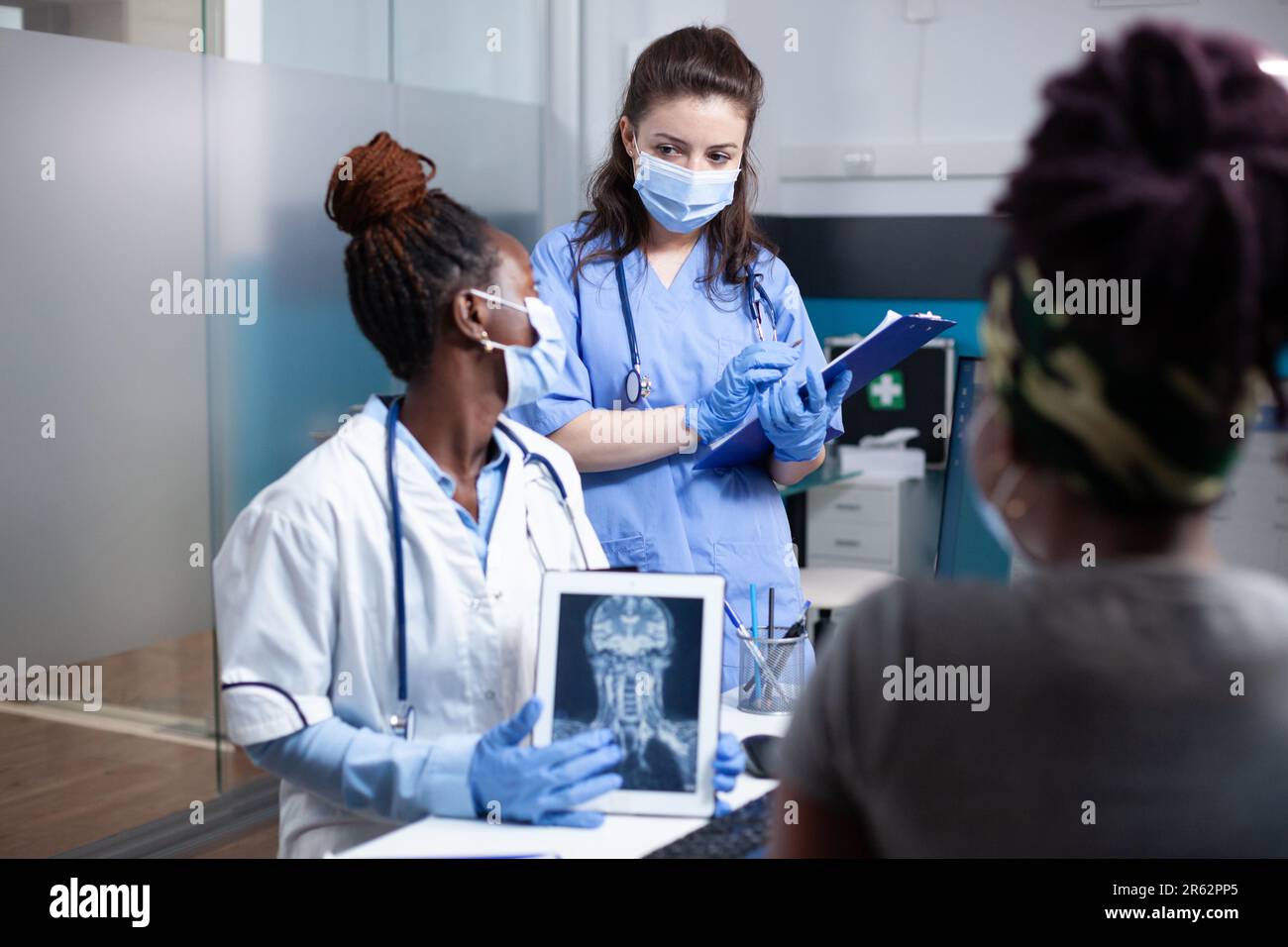 Doctor discussing x-ray ct scan patient cervical spine injury diagnosis results and treatment with nurse during medical appointment. Radiology medical exam in sterile antibacterial clinic environment Stock Photo
