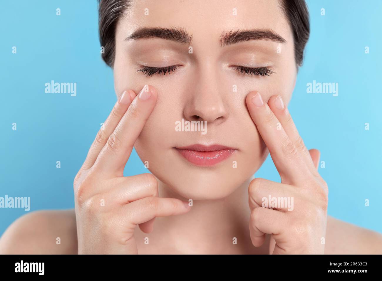 Young woman massaging her face on turquoise background Stock Photo - Alamy