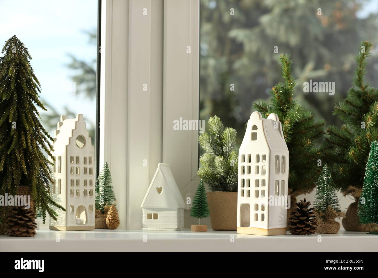 Beautiful house shaped candle holders and small fir trees on windowsill indoors Stock Photo