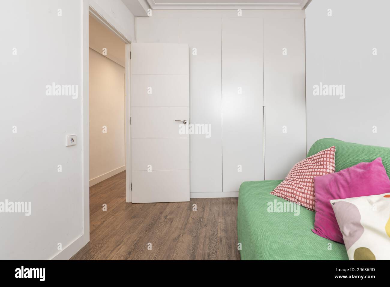 Small room with a green fabric sofa and a wall covered with a built-in wardrobe with white wooden doors Stock Photo