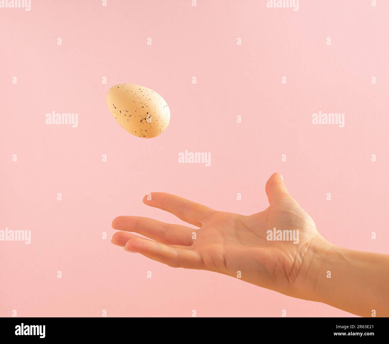 Woman's hand throwing away white egg on pastel pink background. Minimal