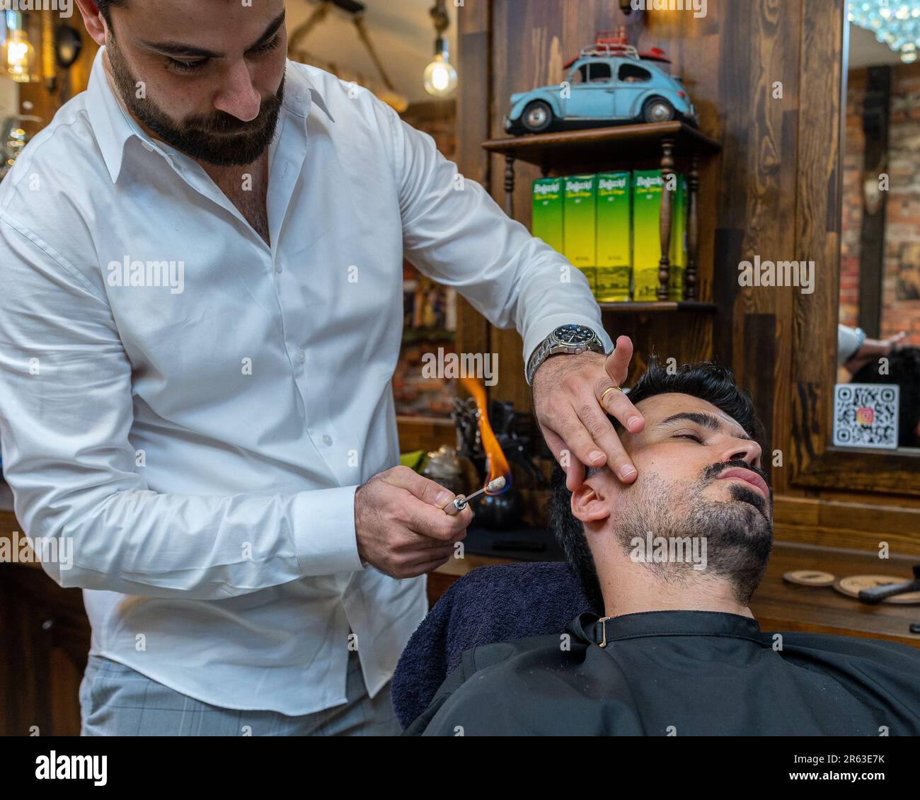 A professional barber styling a customer's hair using a small torch to