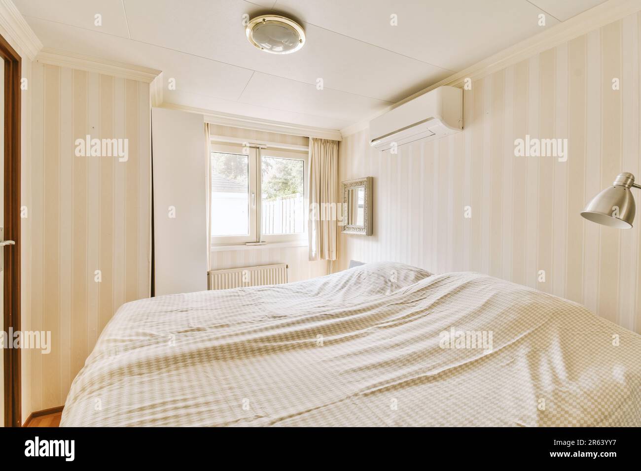a bed in a room with striped wallpaper on the walls and wood flooring around the headboards Stock Photo