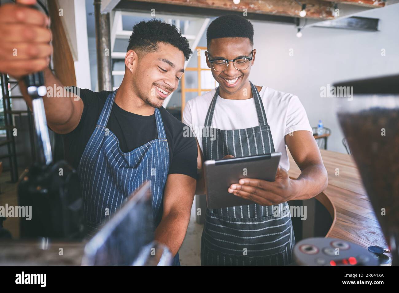 Table number five needs two cappuccinos. two young men using a digital tablet while making coffee at a cafe. Stock Photo