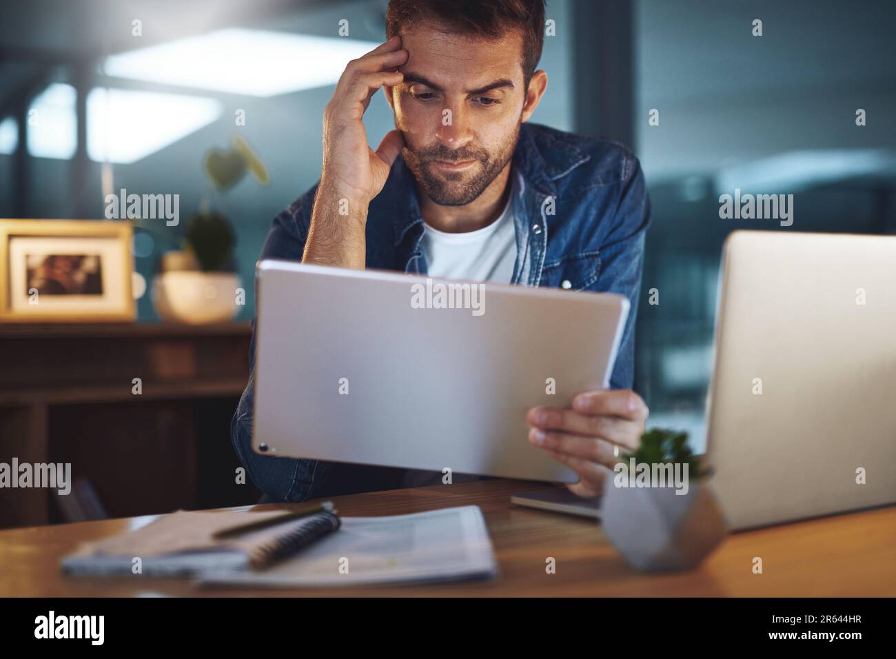 Challenging but I will overcome. a handsome young businessman working late at night on his tablet in a modern office. Stock Photo