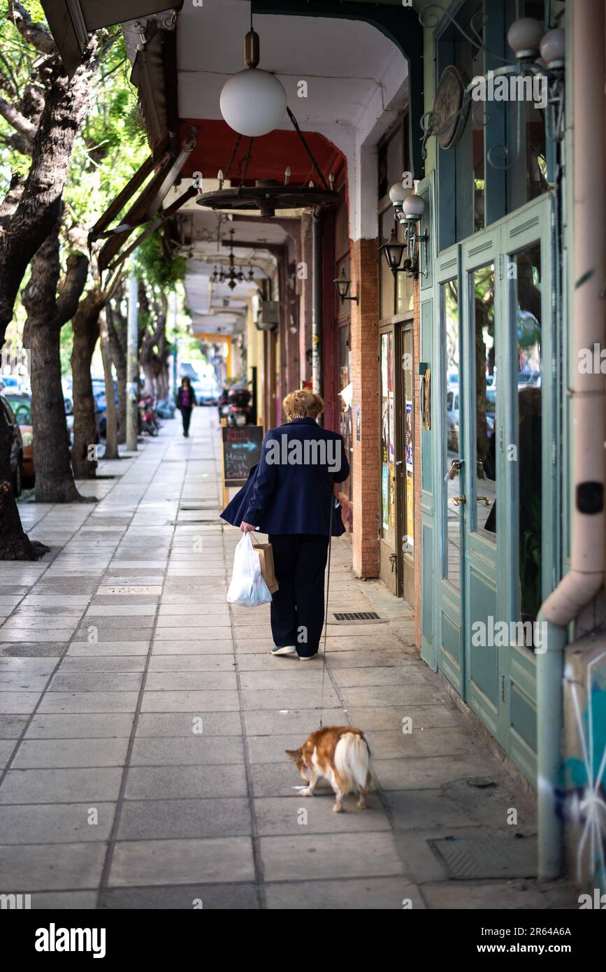 An older woman walking her dog on a street photographed from behind Stock Photo