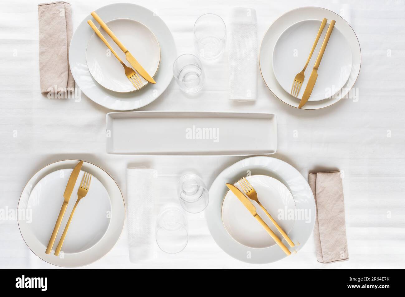 Top view of tableware with linen napkins, gold cutlery and white porcelain plates. Minimalist table settings background for dinner. Stock Photo