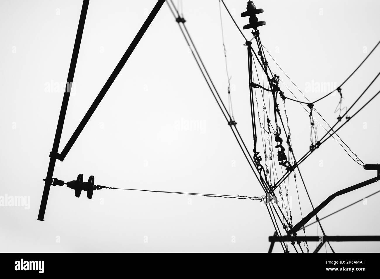 Overhead power lines of a railway are under white sky, monochrome silhouette photo Stock Photo