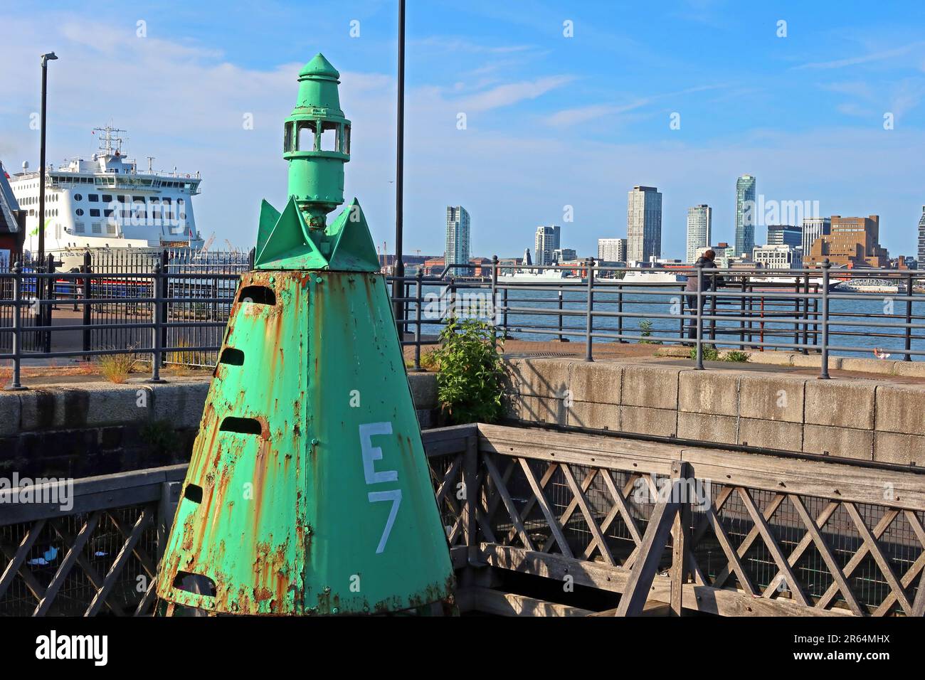 Rusty green E7 navigation buoy on the Birkenhead waterfront, marking the River Mersey shipping channel with the Liverpool skyline visible behind Stock Photo