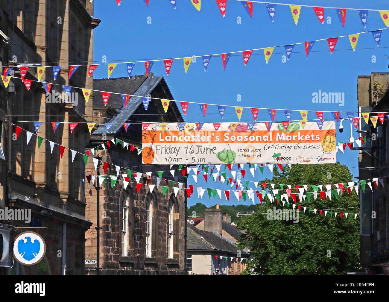 Banner and colourful bunting promoting Lancaster’s seasonal summer markets displayed across a street in Lancaster city centre, Lancashire, England, UK Stock Photo