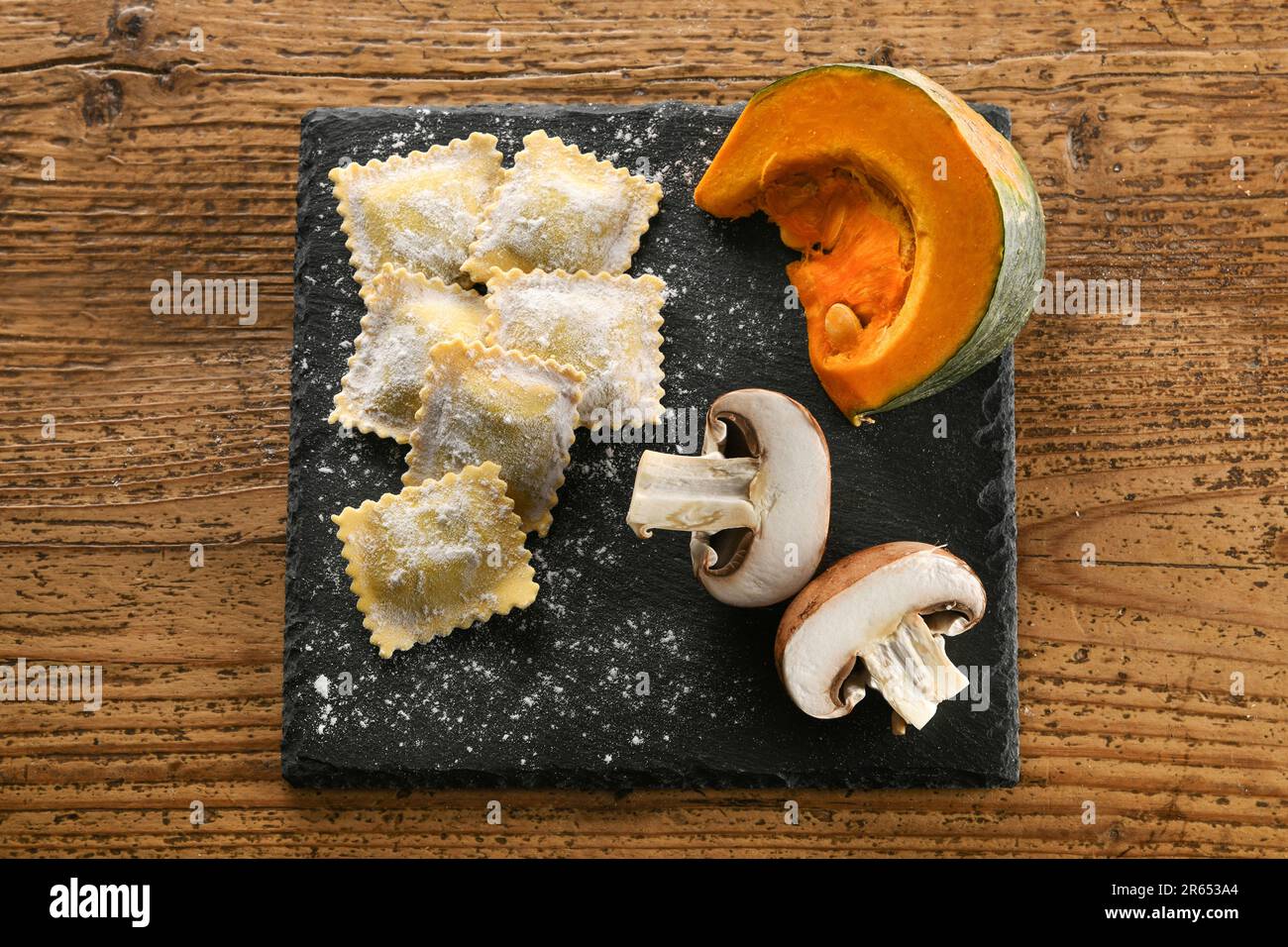 Top view of uncooked Italian ravioli on slate board with aromatic mushrooms and fresh pumpkin placed on wooden table Stock Photo