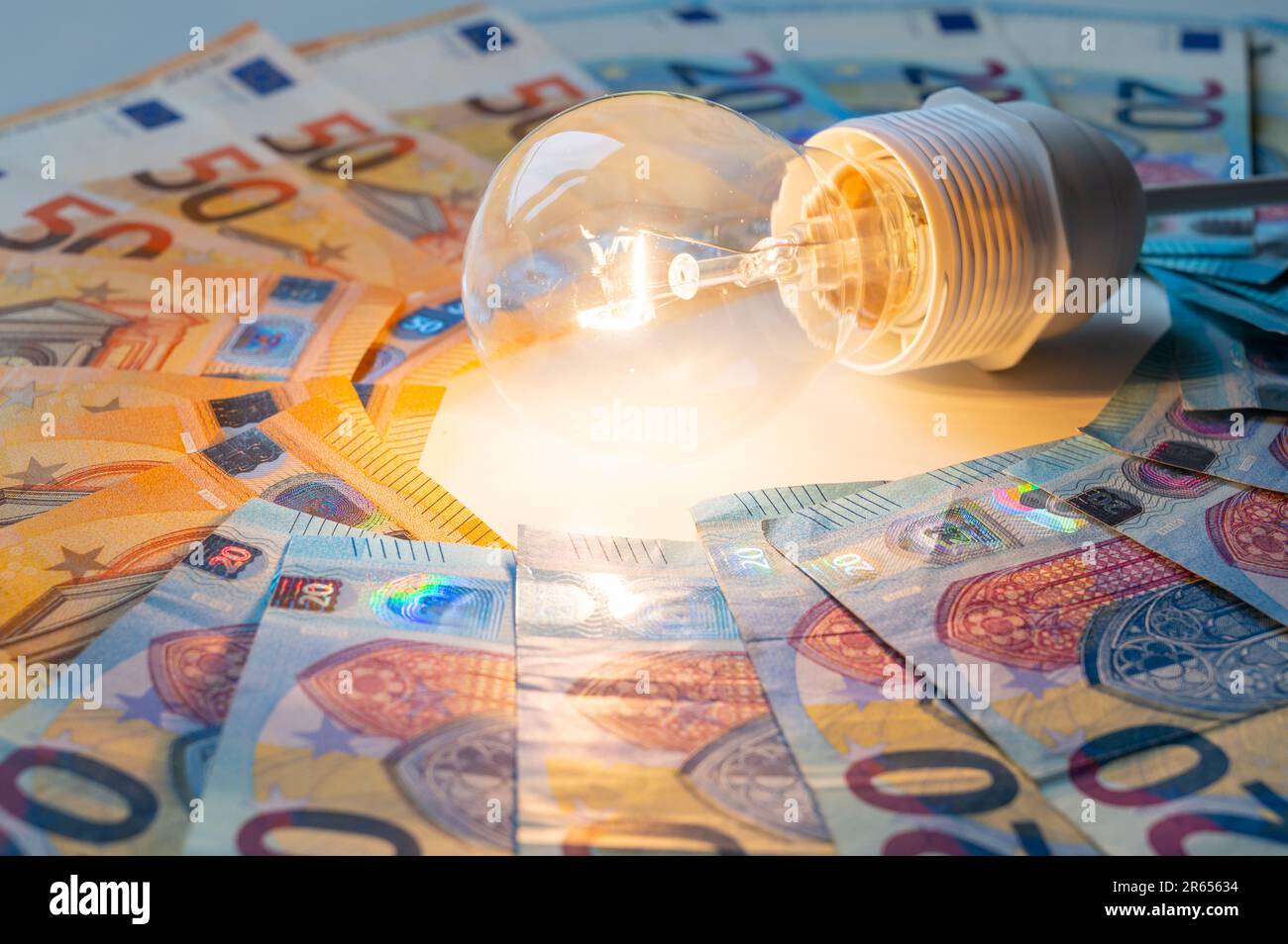 Light bulb turned on, with Euro banknotes around. Increase in electricity tariffs, energy