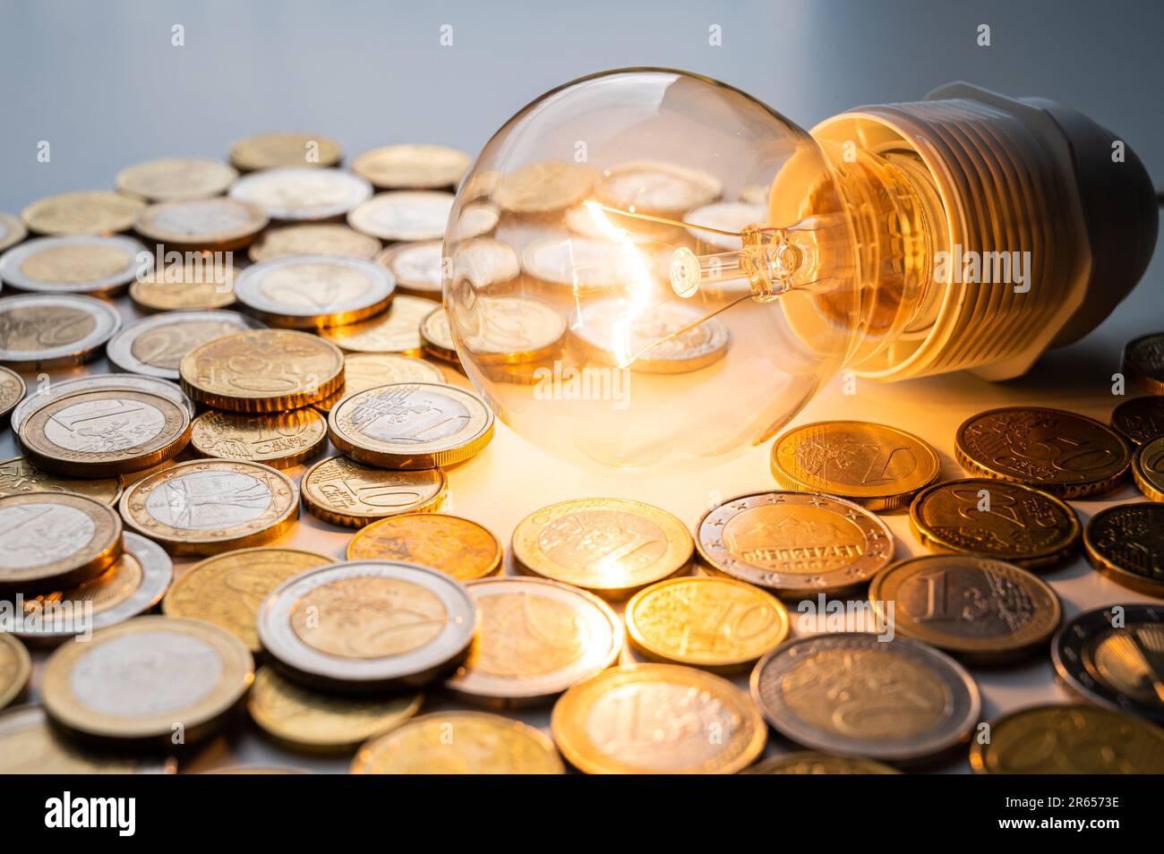 Light bulb turned on, with coins around. Increase in electricity
