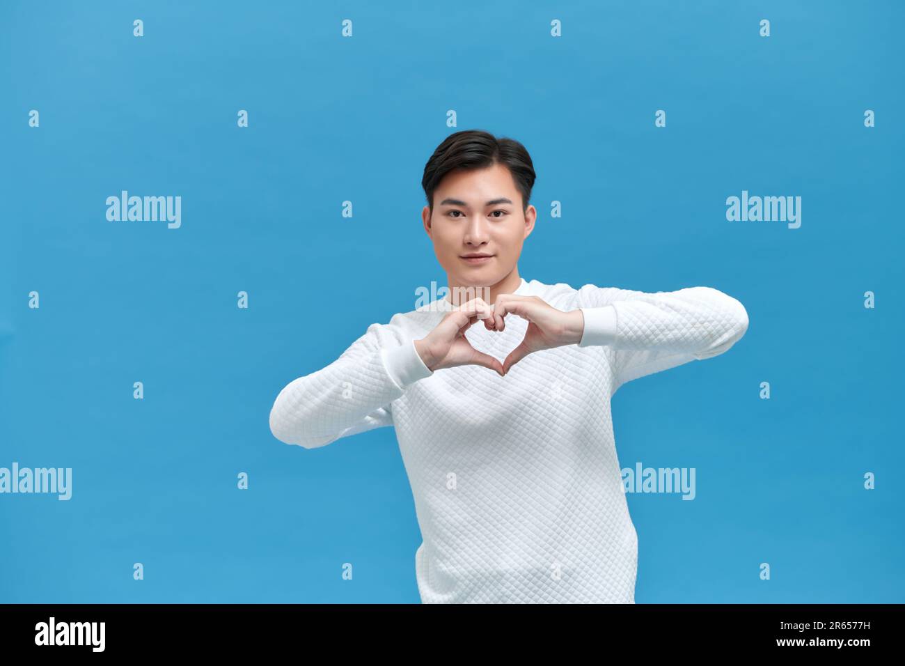 Portrait of attractive Asian man in red t-shirt speaks about own feelings, makes heart gesture over chest, Stock Photo