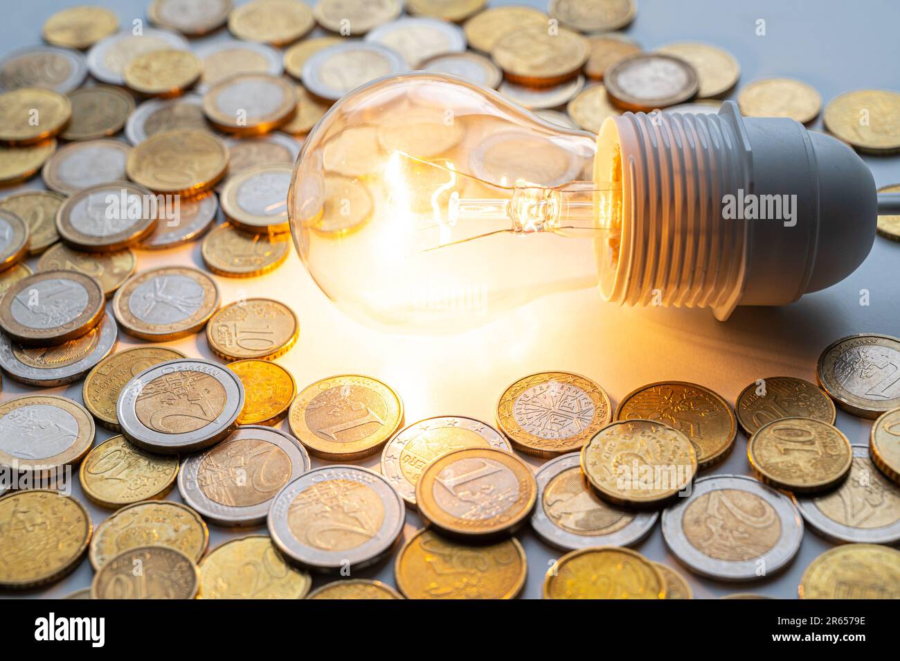 Light bulb turned on, with coins around. Increase in electricity