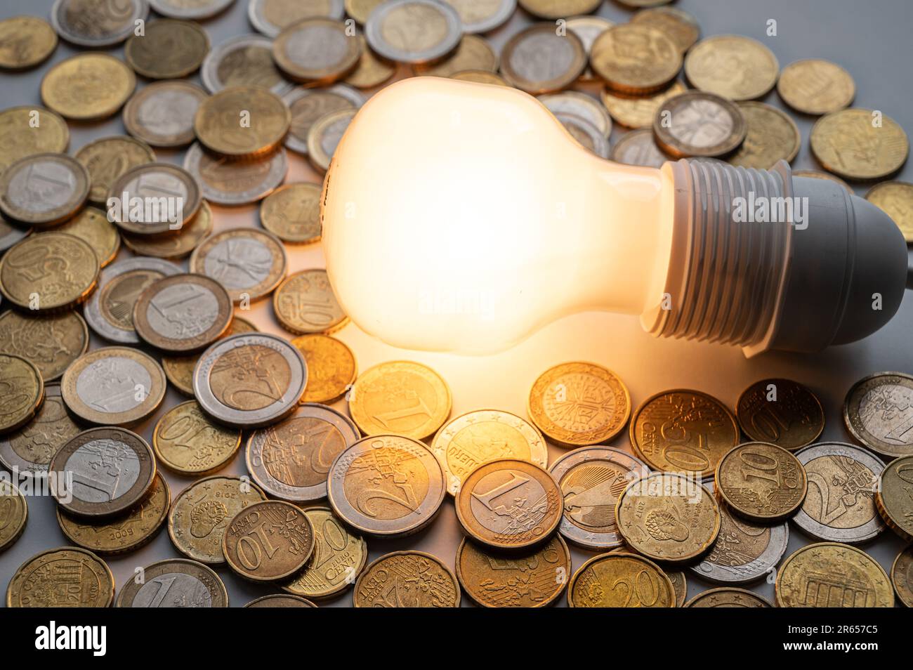 Light bulb turned on, with coins around. Increase in electricity