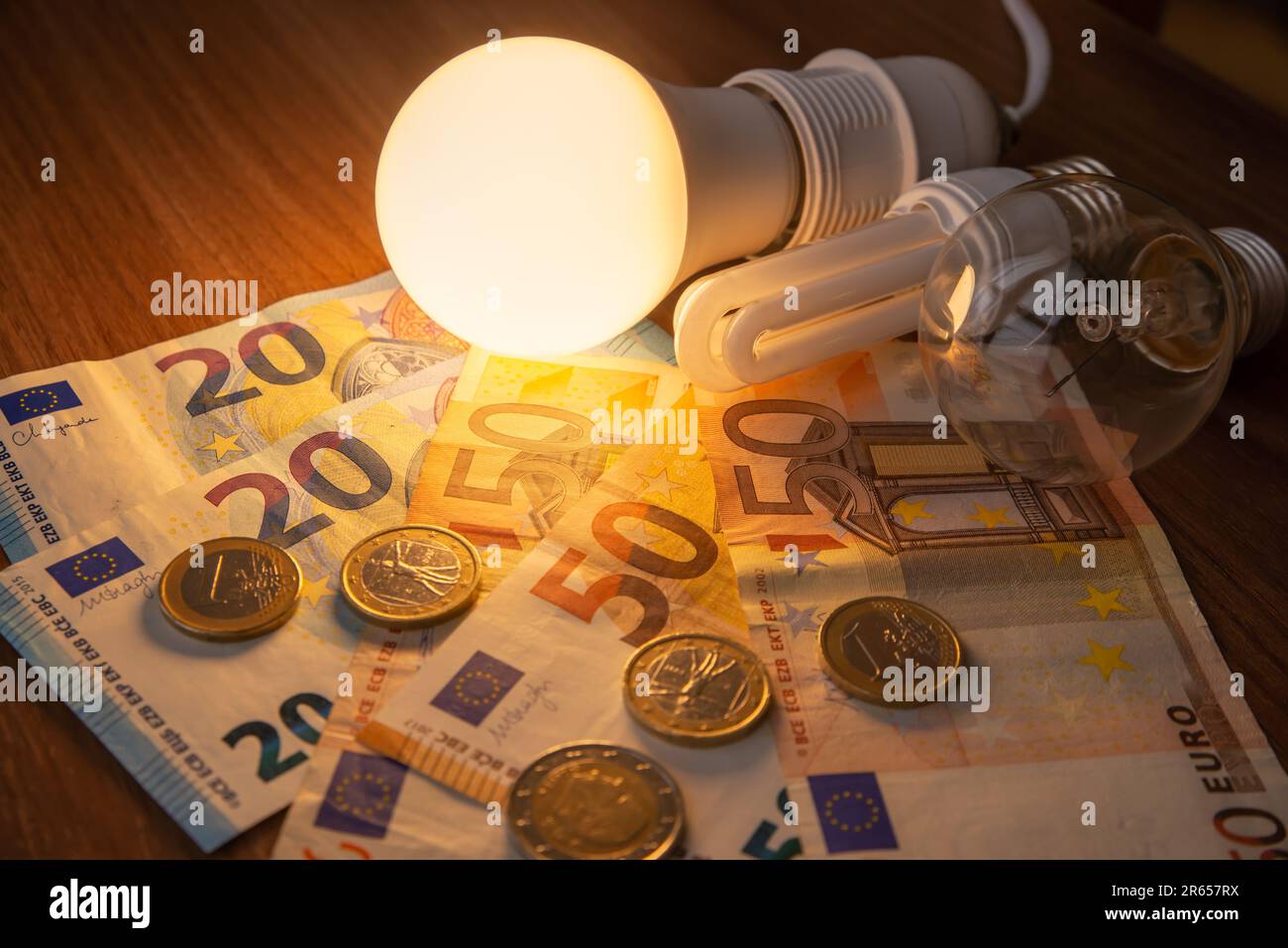 Light bulb lit, with coins and banknotes next to it. Rising electricity