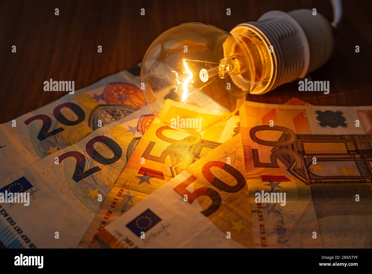 Light bulb lit, with coins and banknotes next to it. Rising electricity