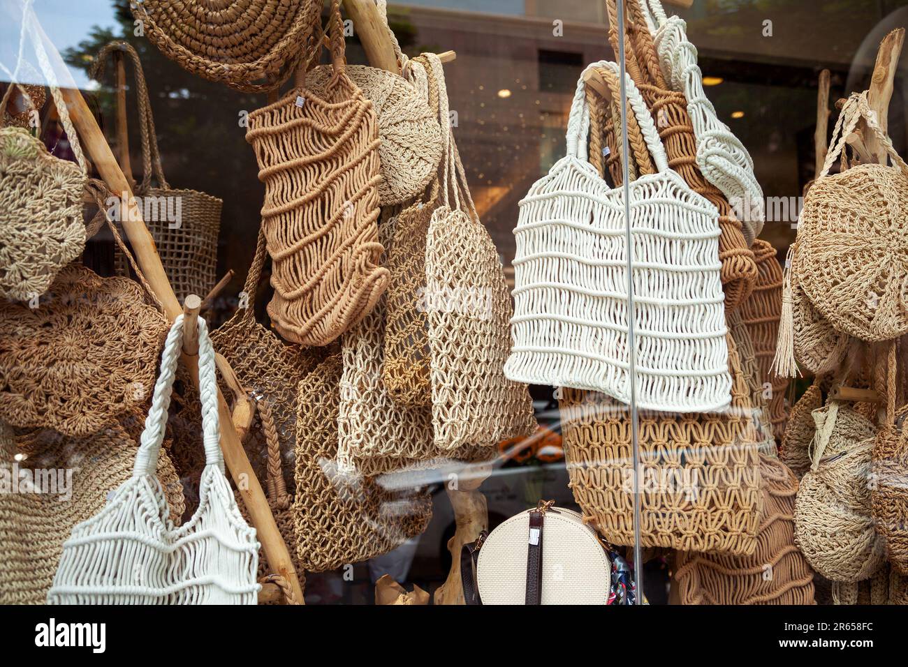 A lot of various woven rope bags in a store window. Various handmade tote bags for sale in a traditional craft shop - Stock Image