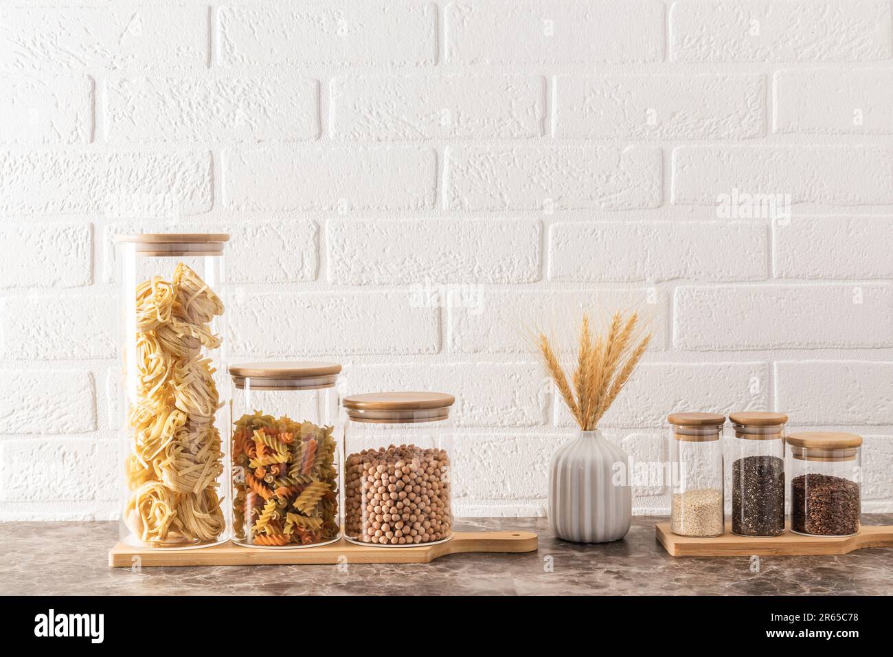 https://c8.alamy.com/comp/2R65C78/compact-stylish-storage-of-bulk-products-in-glass-jars-with-bamboo-lids-front-view-white-brick-wall-kitchen-background-2R65C78.jpg