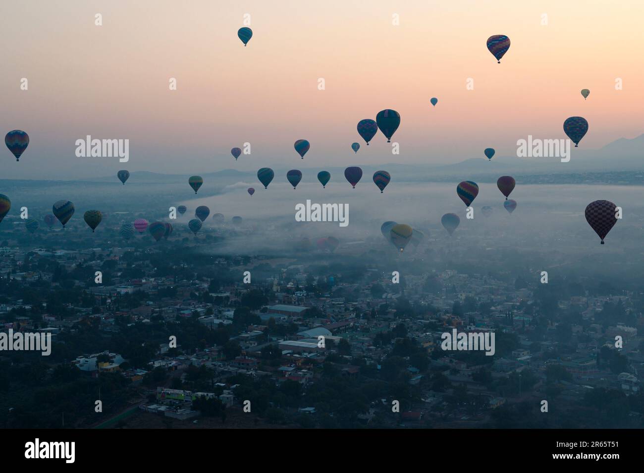 An aerial shot of colorful hot air balloons flying high above the city skyline at sunset. Stock Photo