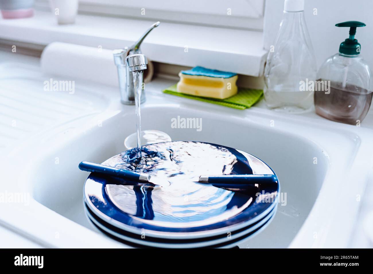 Dirty unwashed blue plates stacked in kitchen sink with flowing tap