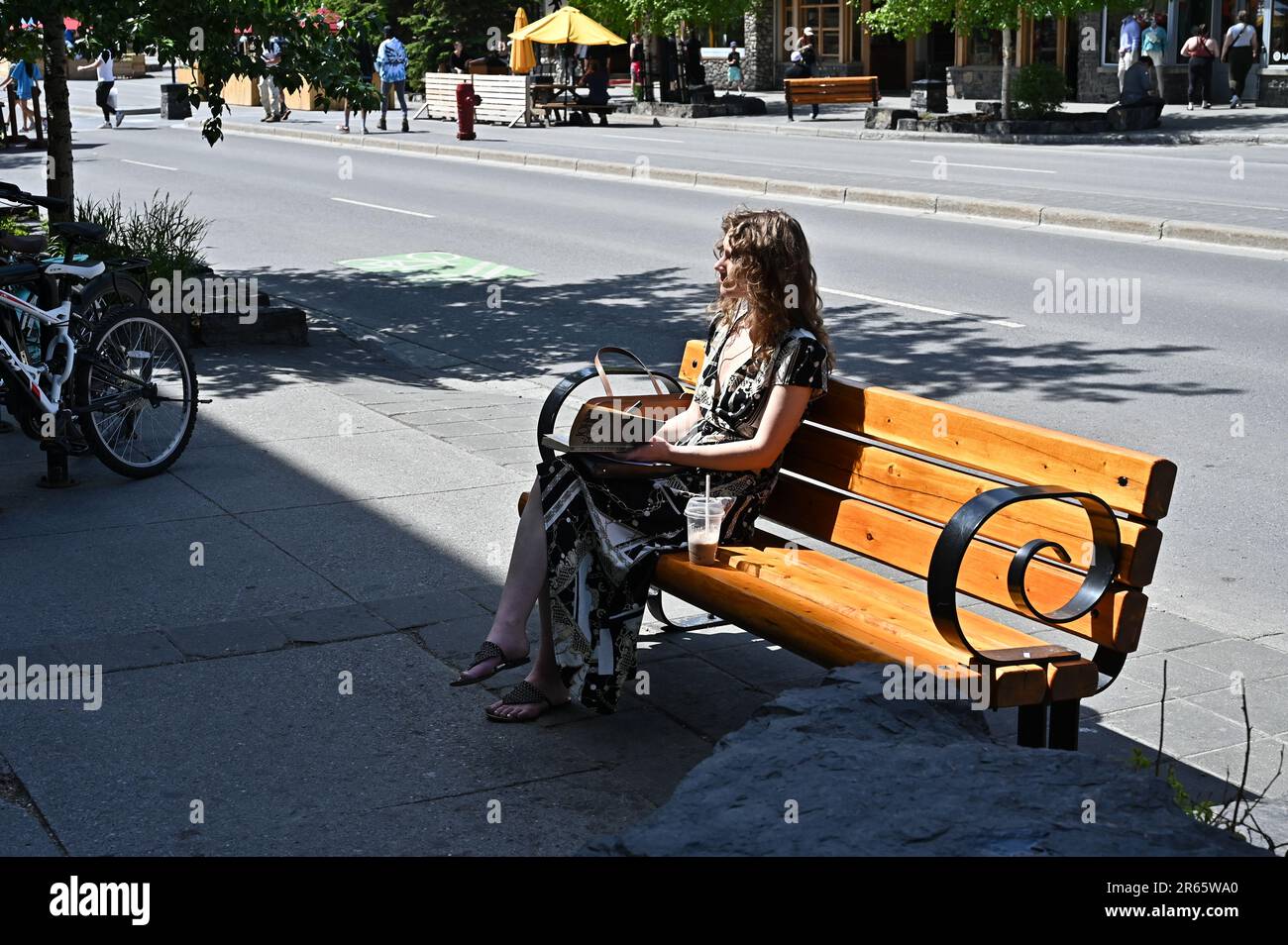 A young female sits on a bench reading a book in Banff, Alberta, Canada ...
