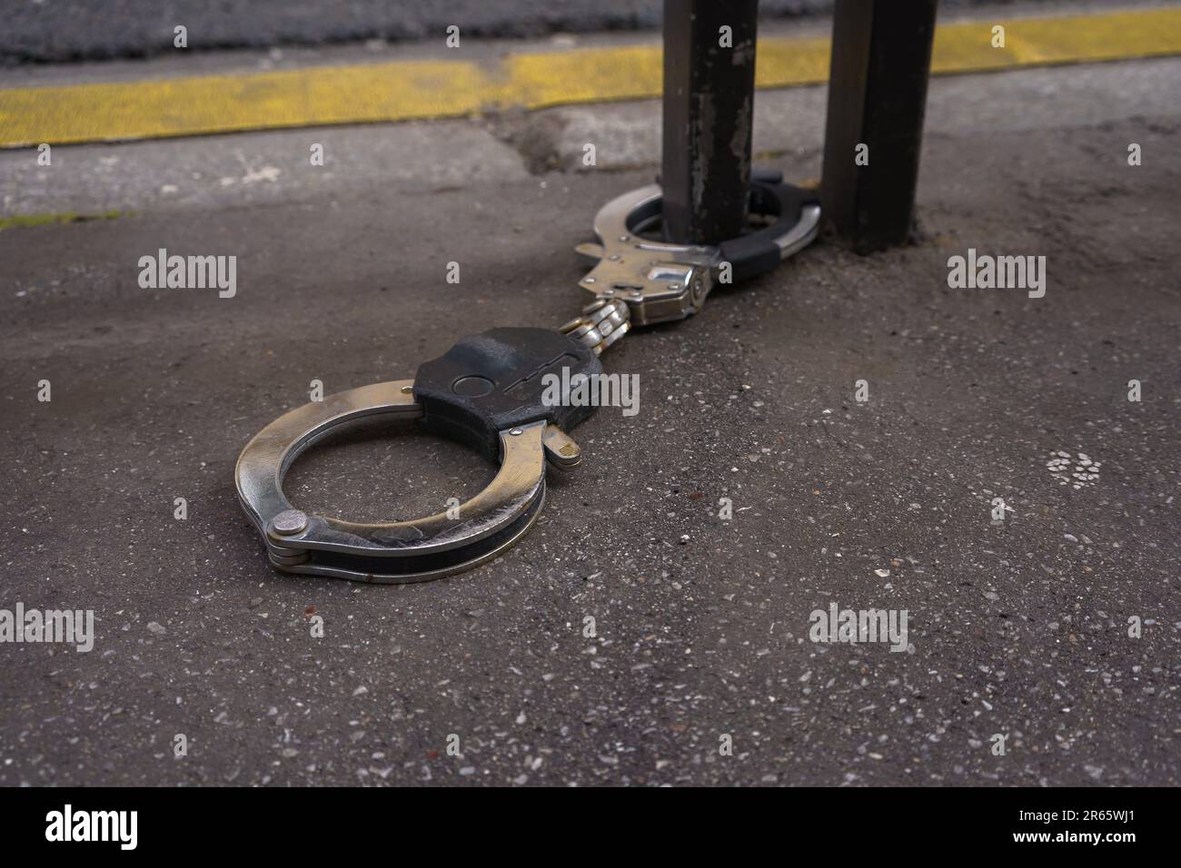 Handcuffs on pavement, attached to a metal railing on the street. Paris, France. Stock Photo