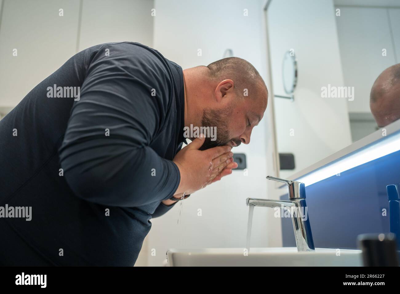 Fat, bald, bearded middle-aged man washes face in bathroom home int sink. Overweight and sweat Stock Photo