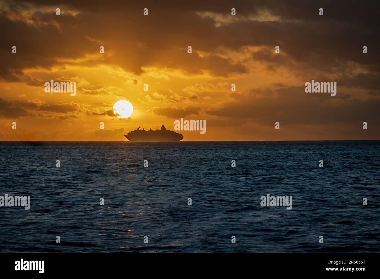 A dramatic shot of a distant ship seen from the deck of a catamaran on a sunset cruise from Bora Bora. Stock Photo