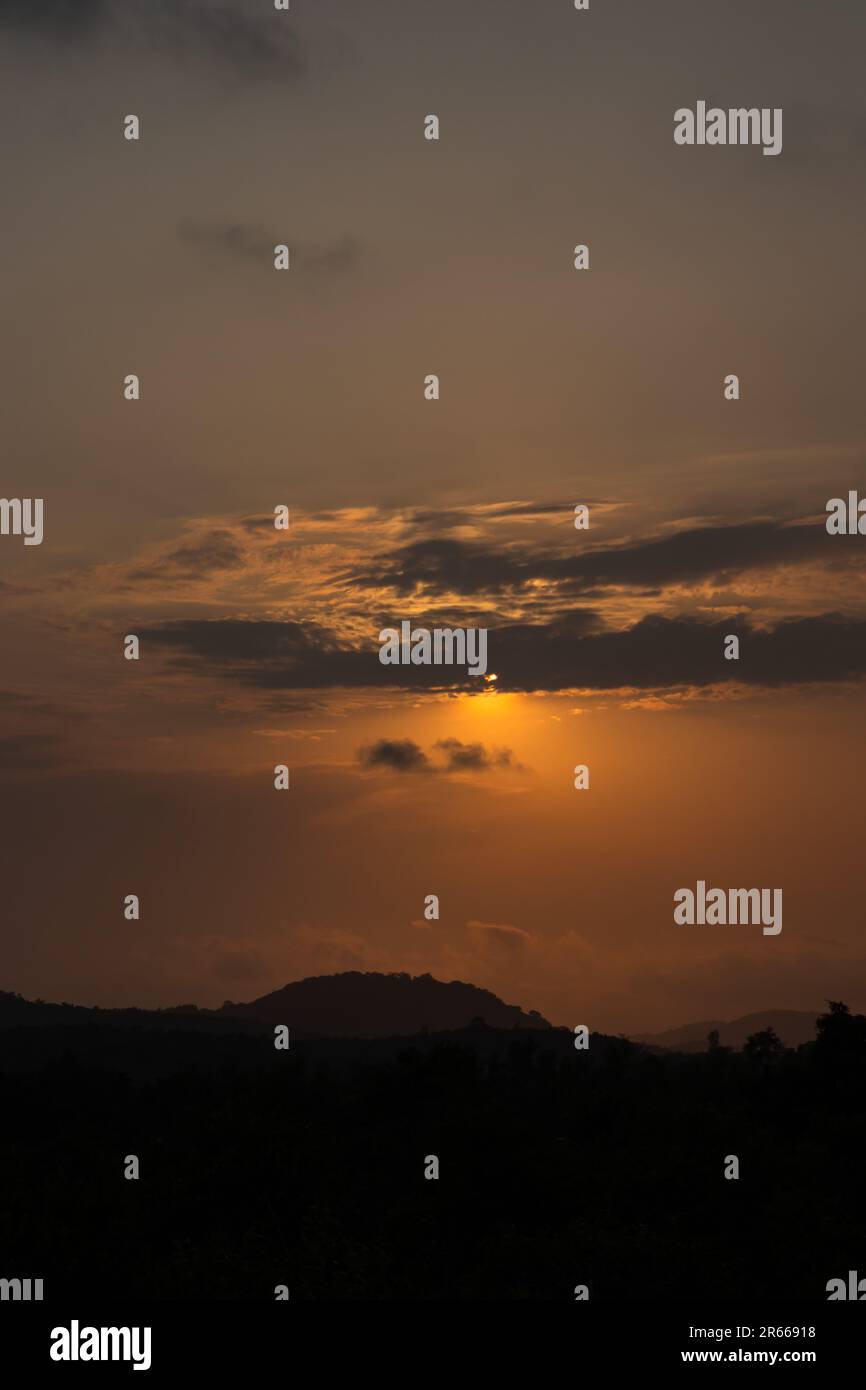 The sun sets, painting the sky in a dramatic orange hue. Silhouetted clouds sit against this tranquil afterglow, creating a breathtakingly beautiful l Stock Photo