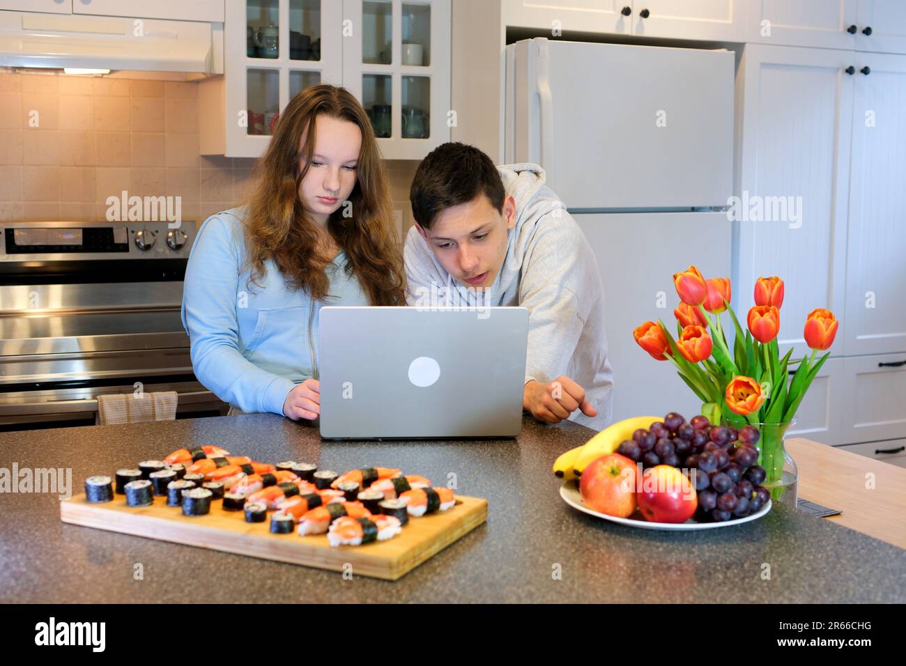 choose movie show set up laptop repair teenagers prepared to watch video sushi on table tulips and fruits in kitchen celebrate valentine's day birthday invite girl to visit movie attentively Stock Photo