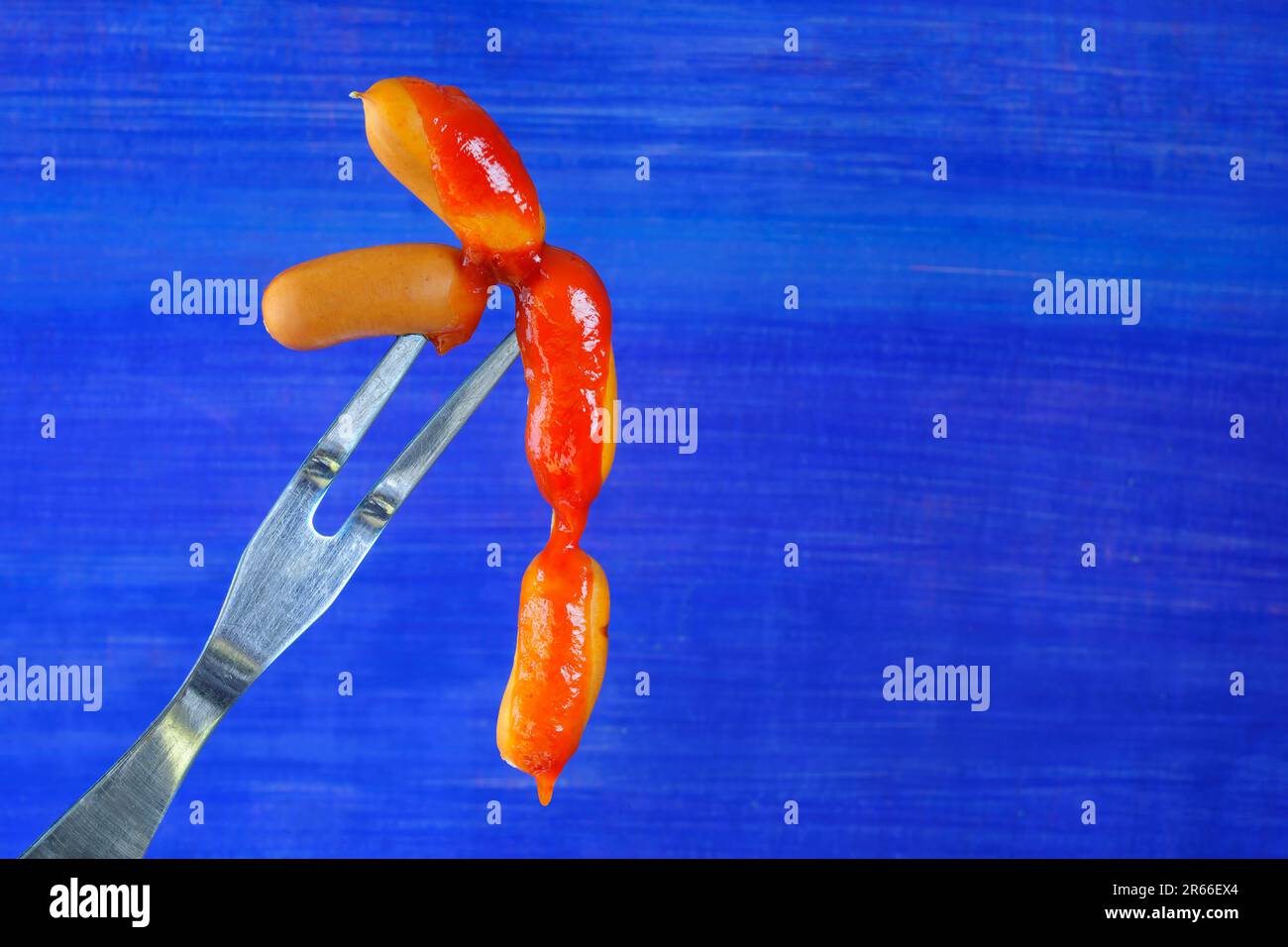 small sausages on vintage fork with dripping ketchup, free copy space, on blue background Stock Photo