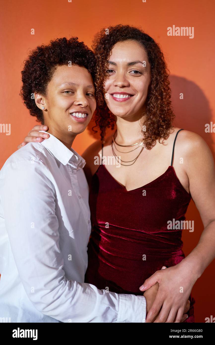 Portrait happy, beautiful lesbian couple hugging on orange background Stock Photo