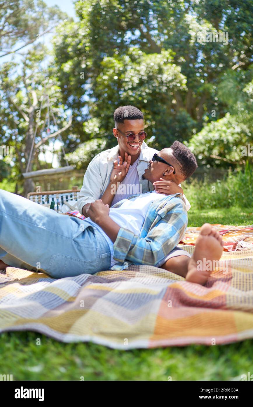 Happy young gay male couple cuddling on picnic blanket in park Stock Photo