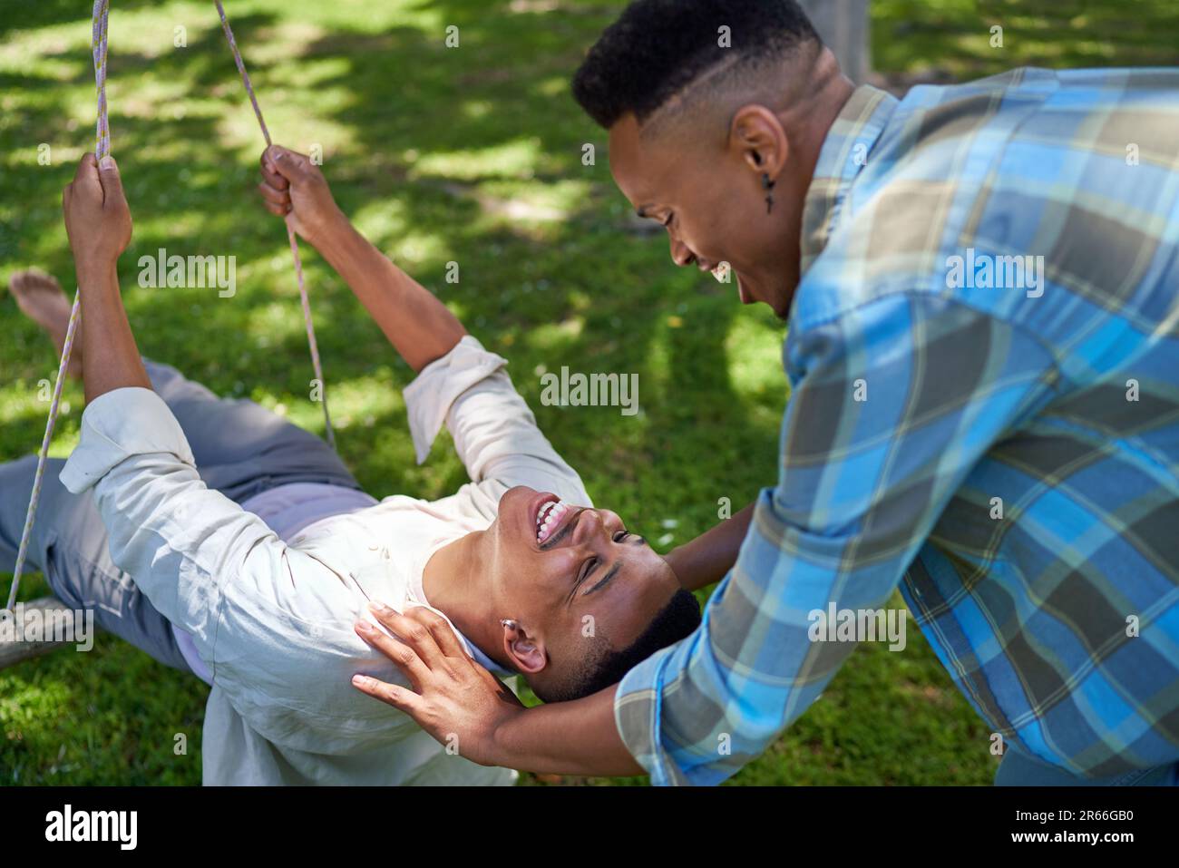 Happy young gay male couple on swing in summer park Stock Photo