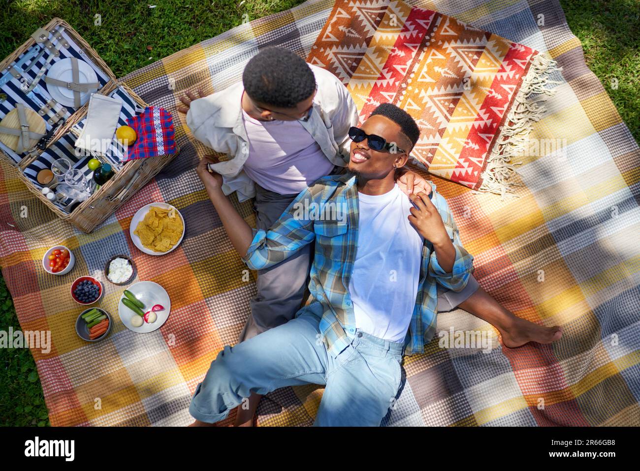 Young gay male couple cuddling, enjoying picnic on blanket in park Stock Photo