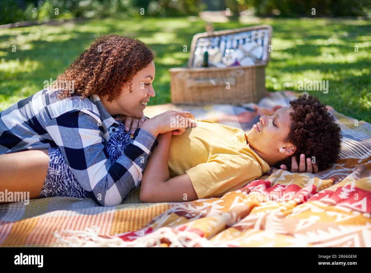 Happy lesbian couple relaxing, laying on picnic blanket in summer park Stock Photo