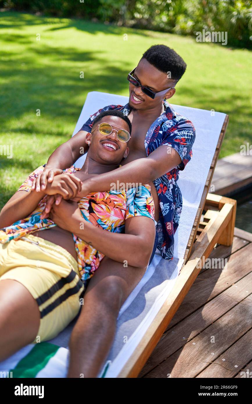 Happy young gay male couple cuddling, relaxing on lounge chair Stock Photo