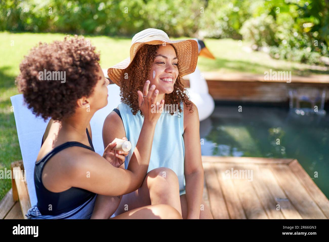 Happy lesbian couple applying sunscreen to face at summer poolside Stock Photo