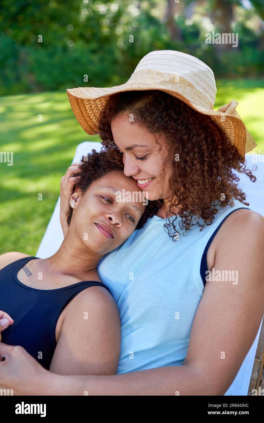 Happy, affectionate lesbian couple cuddling in summer backyard Stock Photo