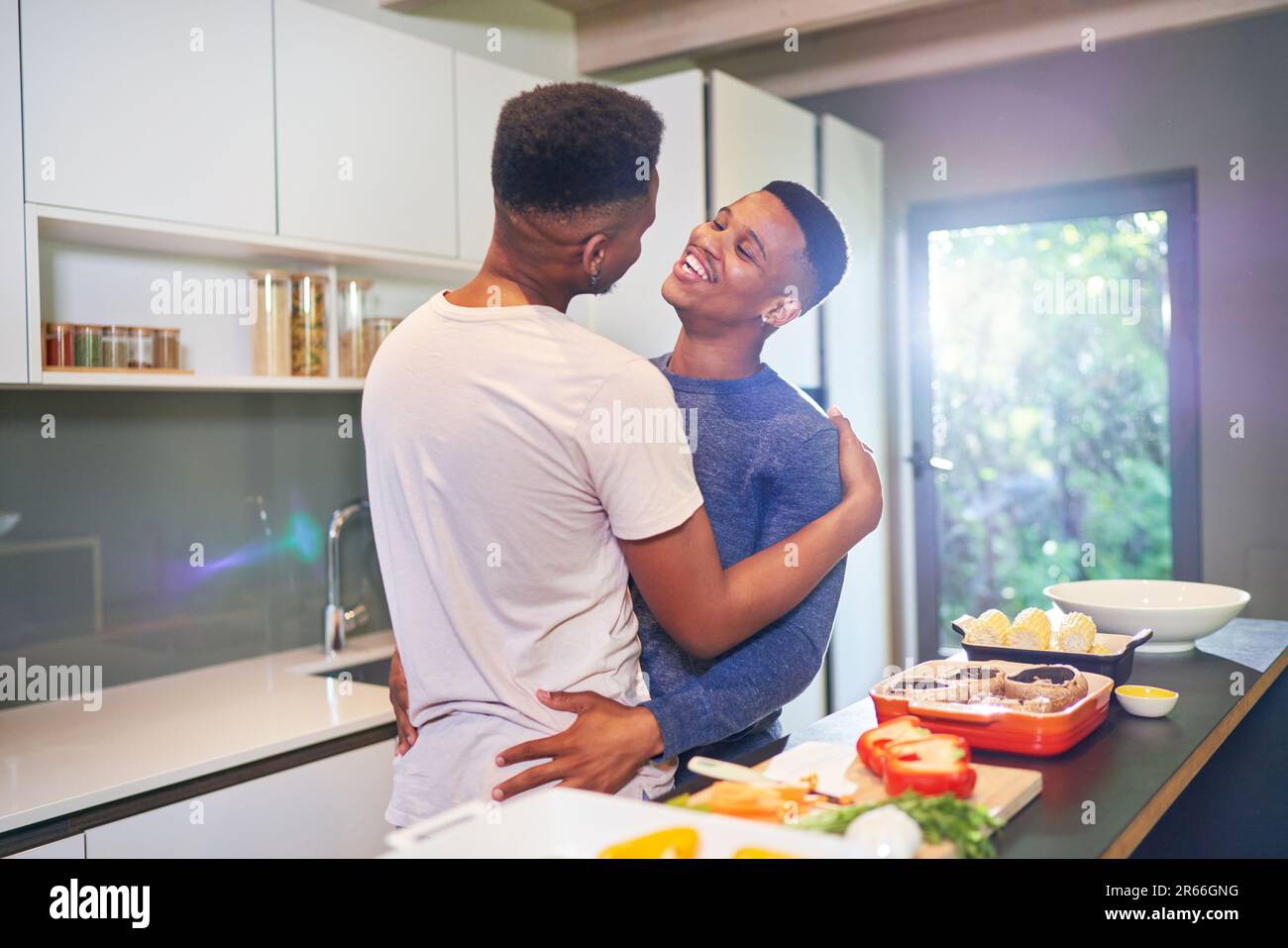 Happy, affectionate young gay male couple hugging and cooking at home Stock Photo