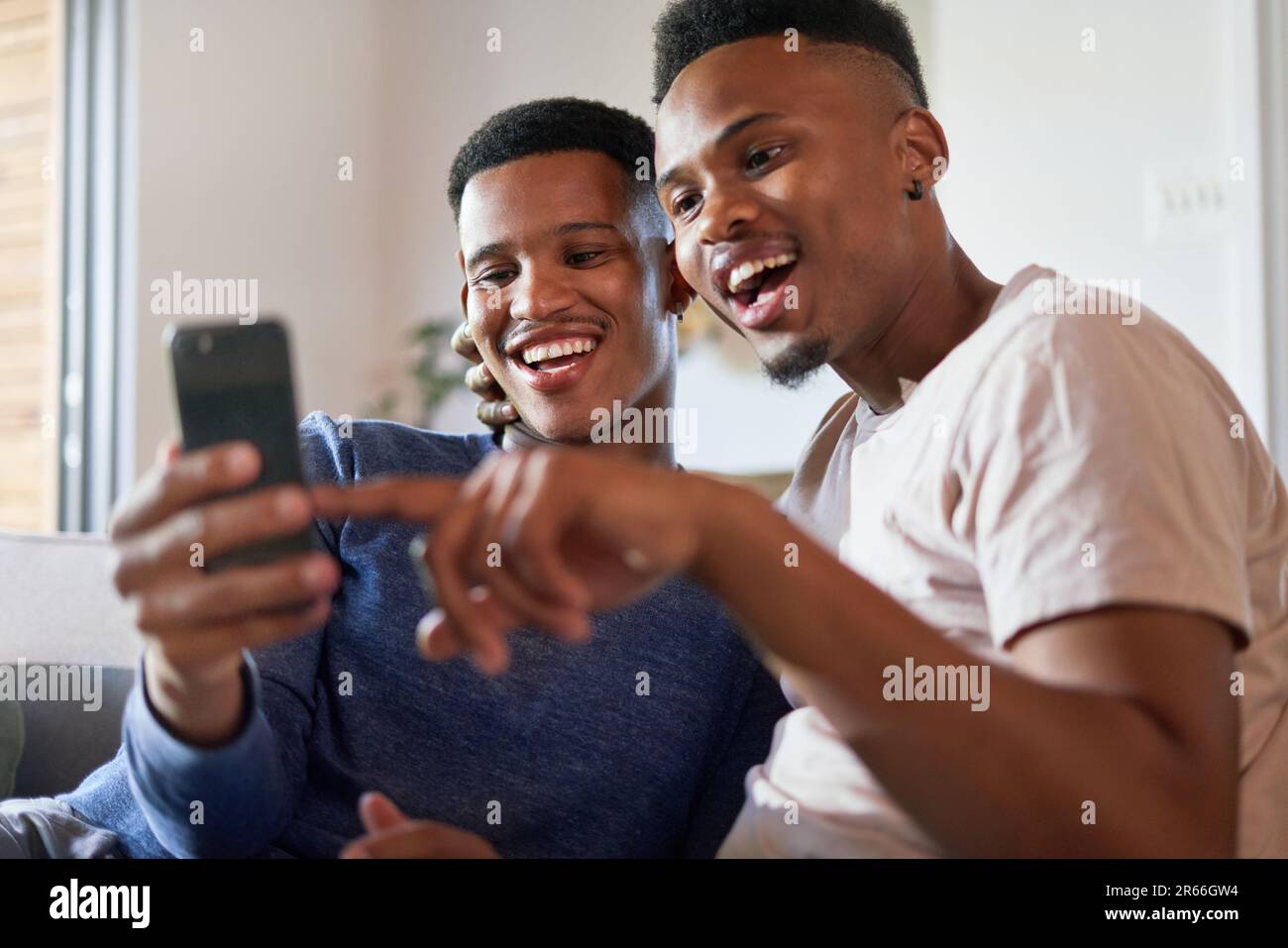 Happy young gay male couple using smart phone at home Stock Photo