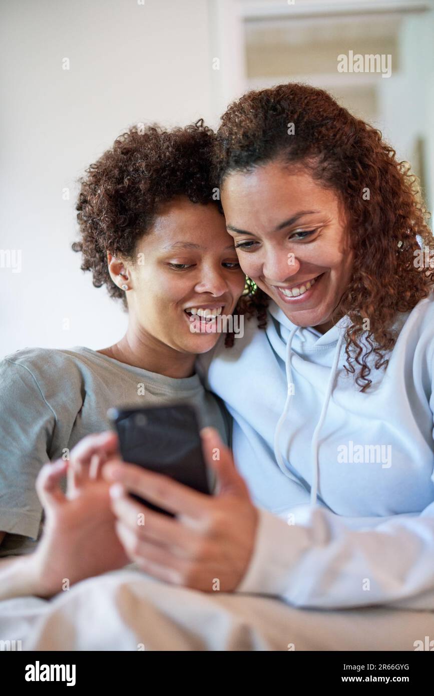 Happy lesbian couple using smart phone together at home Stock Photo