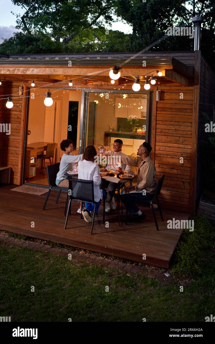 Gay couples enjoying dinner at table on patio with string lights Stock Photo