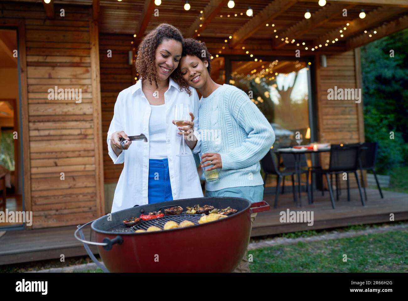 Happy, affectionate lesbian couple barbecuing in summer backyard Stock Photo