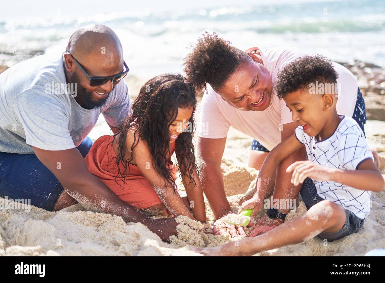Happy gay male couple with kids playing in sand on sunny beach Stock Photo
